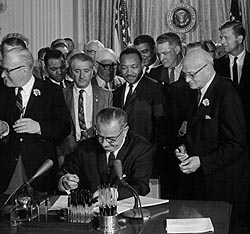 President Lyndon Johnson signing the Civil Rights Act of 1964 into law, with Martin Luther King, Jr., looking on.